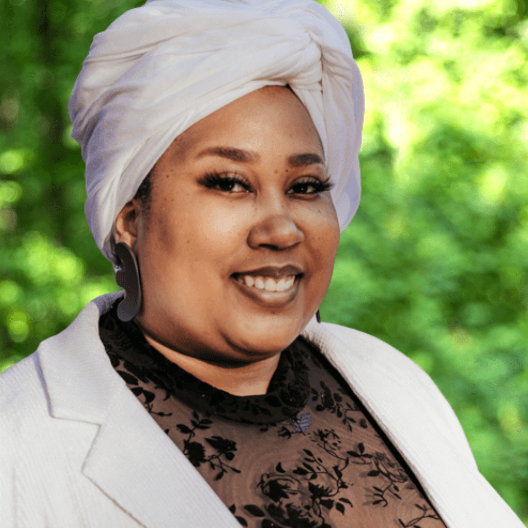 Alysha Suryah headshot. Woman smiling, white headwrap and blazer with black top.