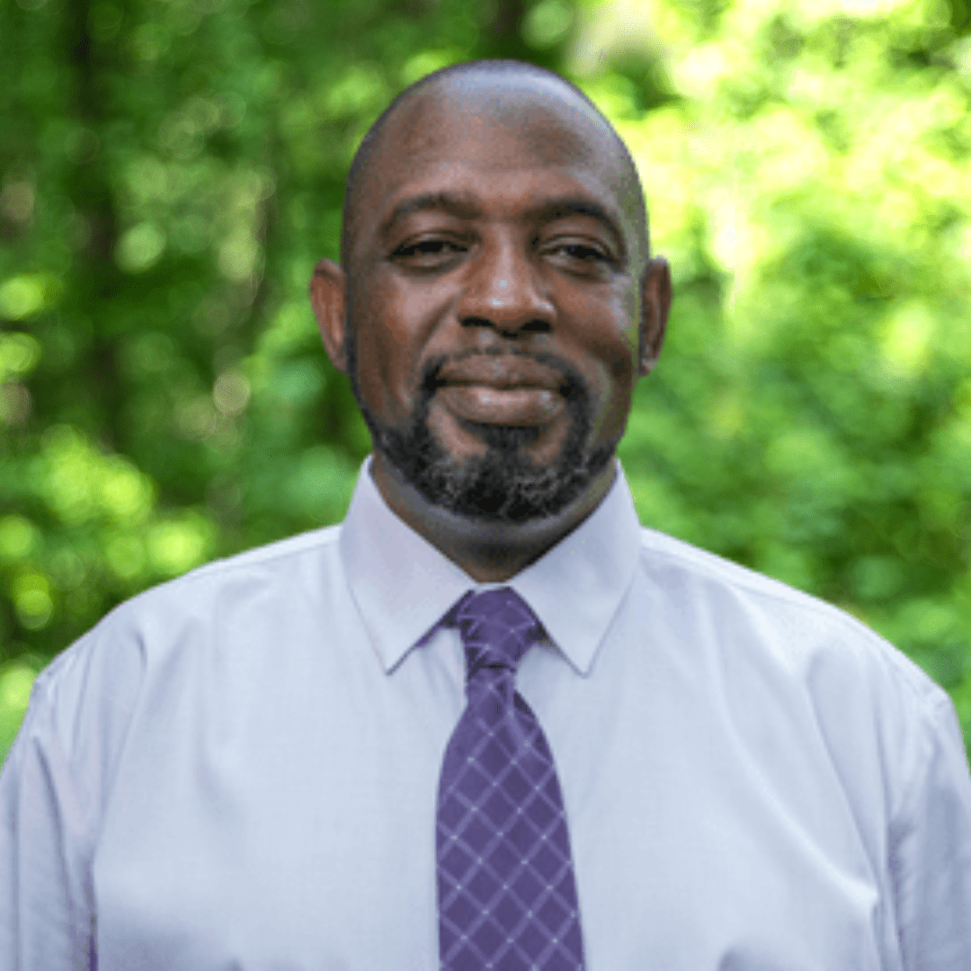 Headshot of David Mitchell. Man smiling with light blue collared shirt and purple necktie. 
