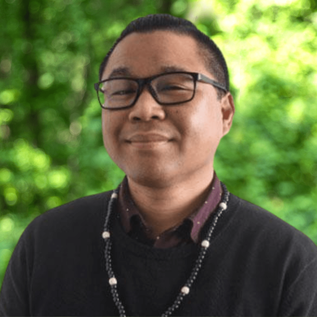 Headshot of Derrick Quevedo. Man with glasses smiling with dark shirt and black necklace