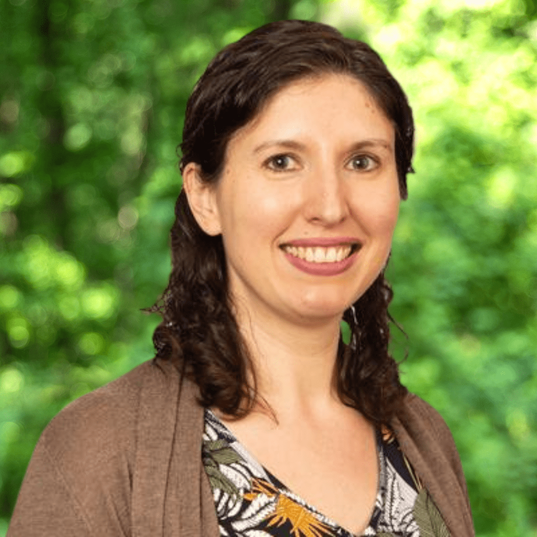 Smiling woman with dark, shoulder-length hair, a patterned top, and a brown sweater.
