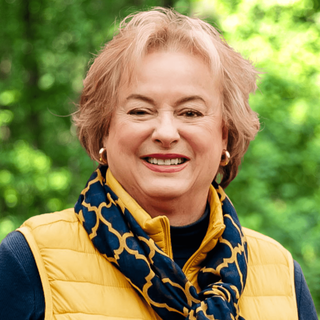 headshot of Midge Ingersoll. Woman smiling with short blonde hair and a yellow puffer vest with a black and yellow scarf