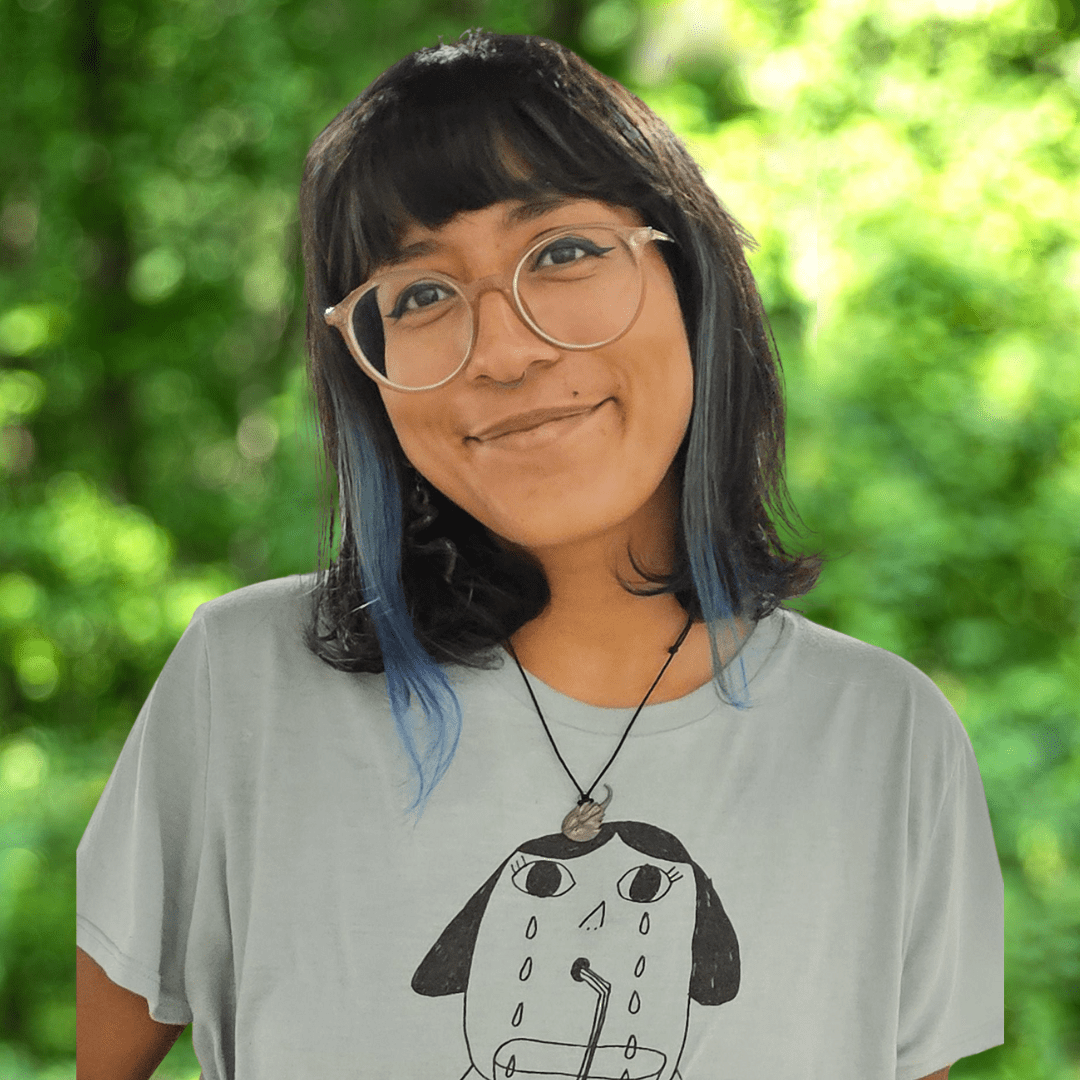 headshot of elli maria. woman in graphic tee, eye glasses and multicolor hair smiling to camera