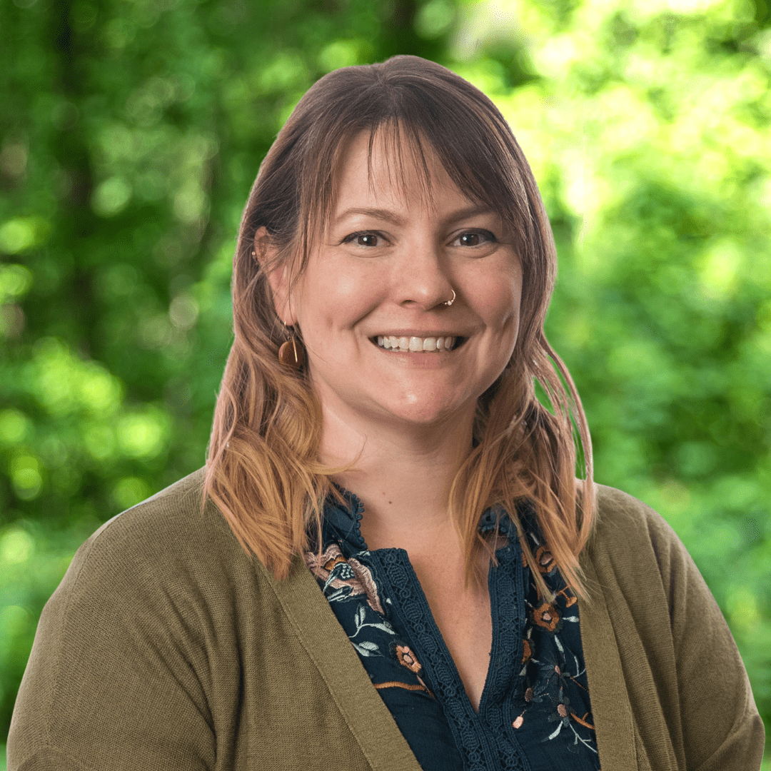 Jess Porter headshot. Woman with shoulder length hair, dark shirt and olive sweater,, smiling.