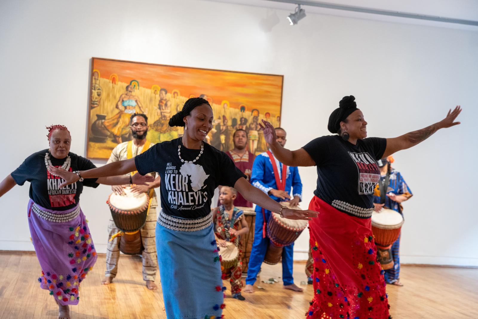 3 dancers performing to live drum circle behind them.