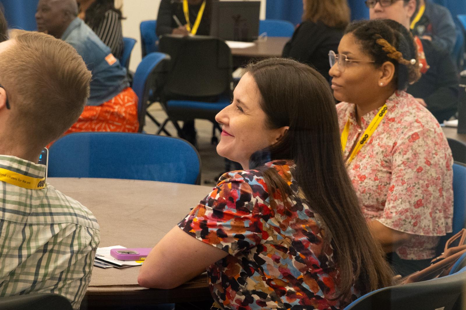 Women smiling sitting at round table with others. 